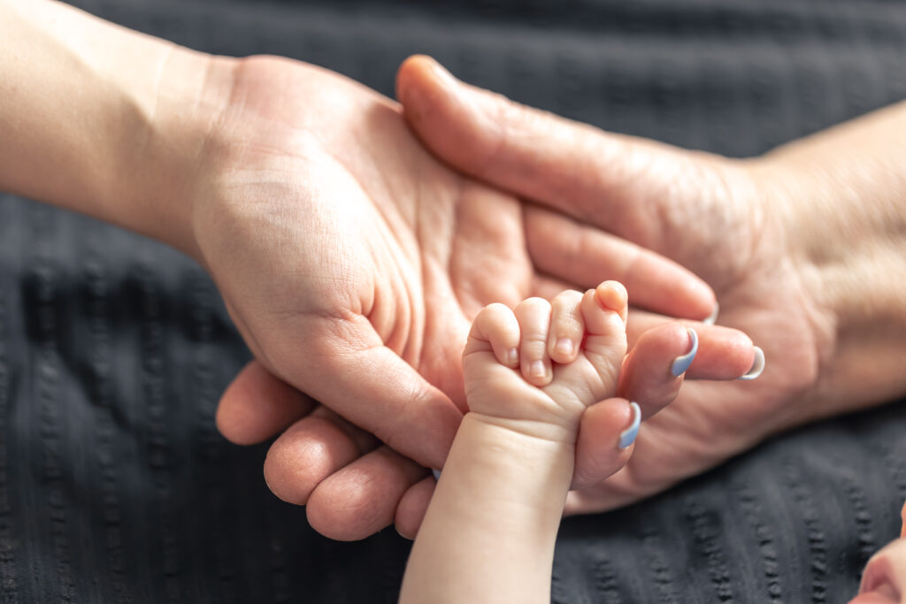 A parent's hand gently holding a small baby's foot, symbolizing care and concern for infant health.