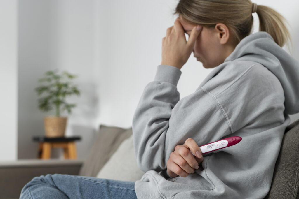 A sad woman holding a negative pregnancy test while covering her face.